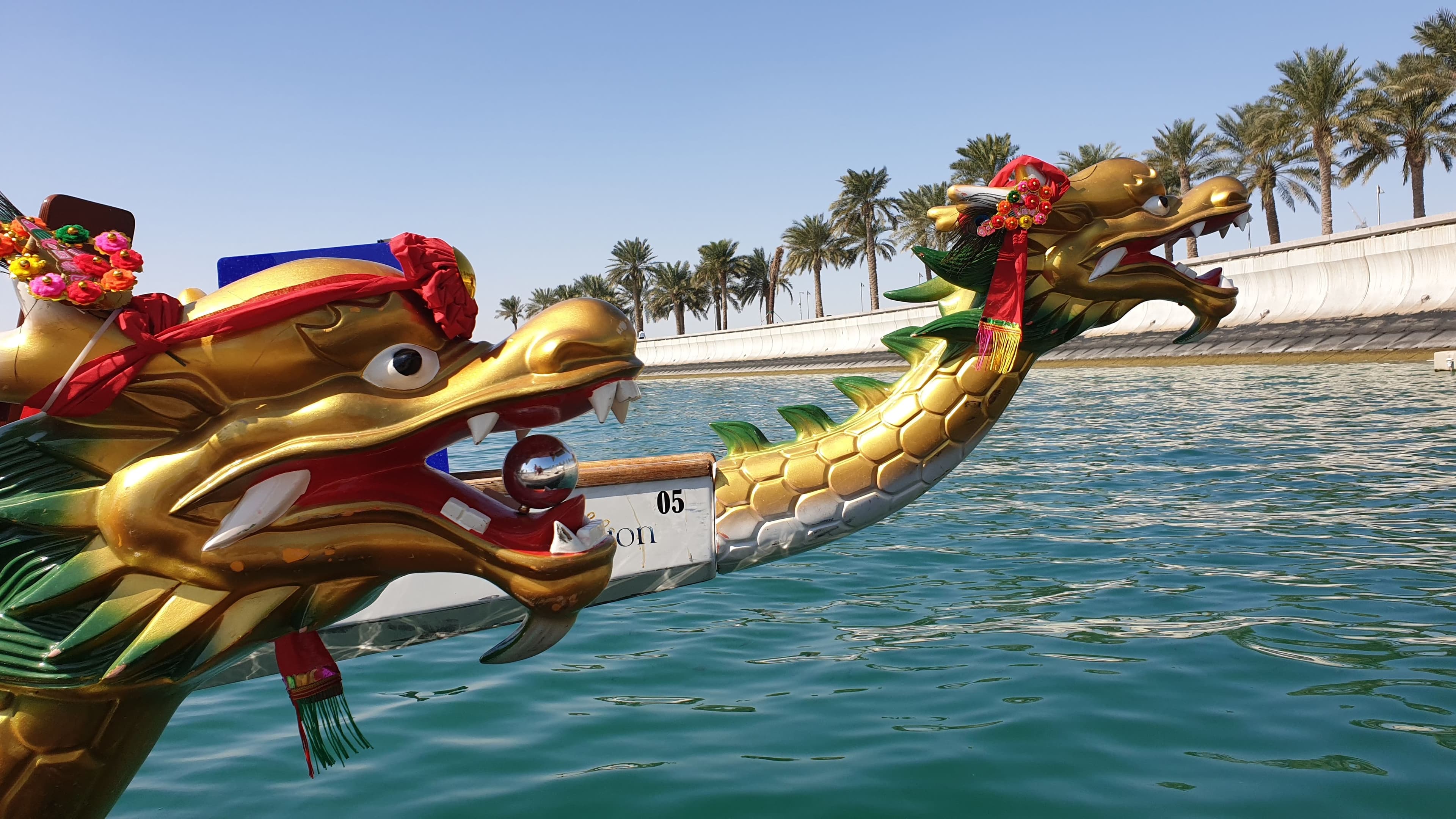 The carved gold dragon heads of two dragon boats side by side on the water